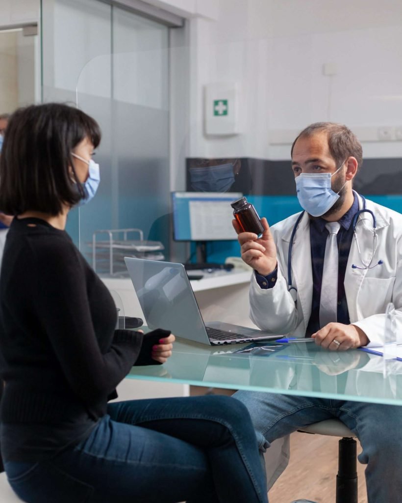 Specialist giving bottle of prescription pills to patient for treatment, doing checkup consultation in cabinet. Woman receiving flask of medicaments from medic during covid 19 pandemic.